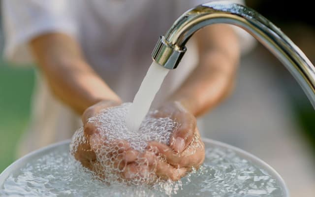 Niño acumulando agua dura con las manos bajo un grifo